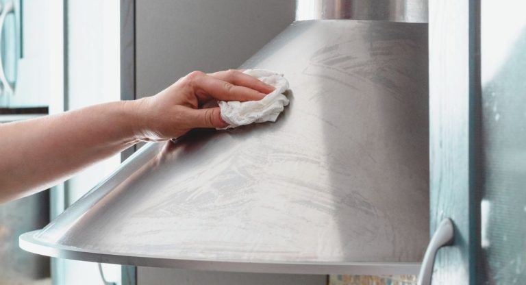 Main nettoyant une hotte de cuisine en inox avec un chiffon