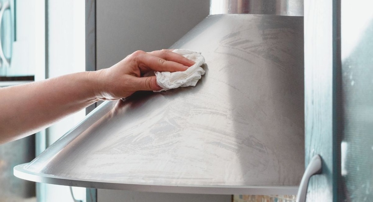 Main nettoyant une hotte de cuisine en inox avec un chiffon