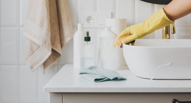 Personne nettoyant un lavabo de salle de bain avec gant et eponge