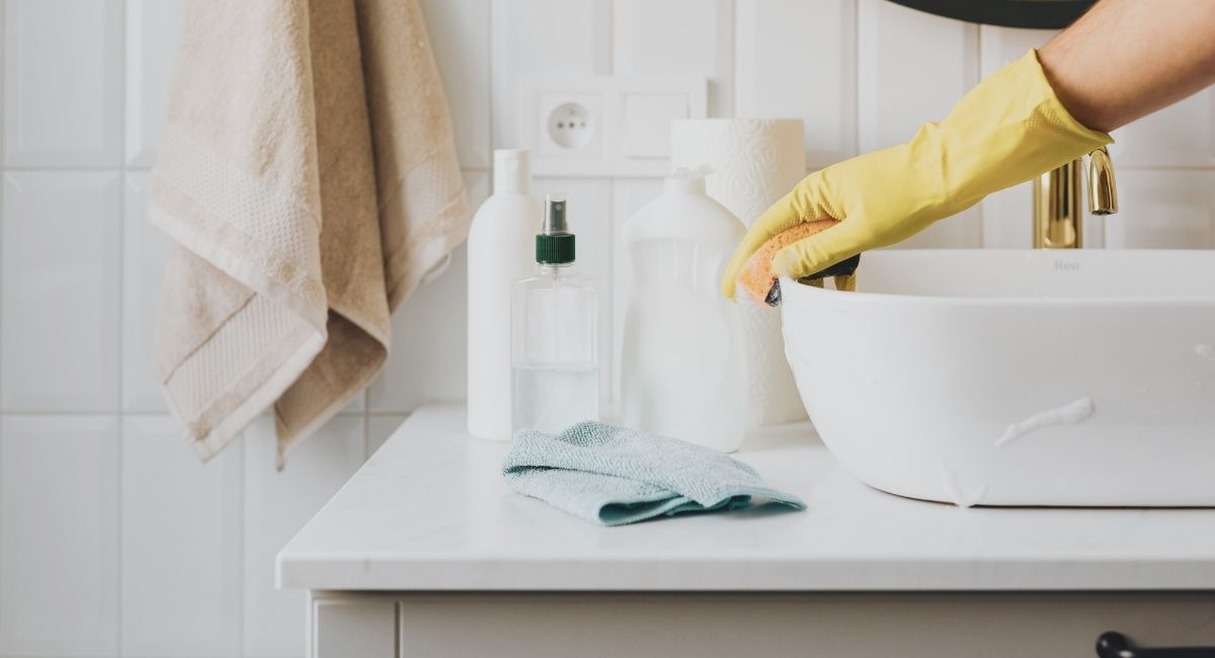 Personne nettoyant un lavabo de salle de bain avec gant et eponge